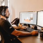 Profissional usando fones de ouvido e trabalhando em um computador com dois monitores em um escritório moderno