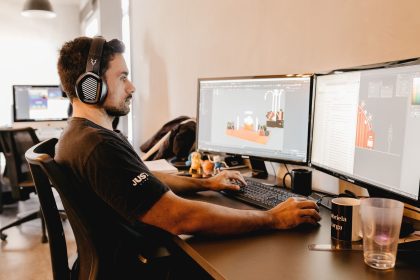 Profissional usando fones de ouvido e trabalhando em um computador com dois monitores em um escritório moderno