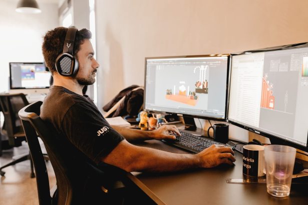 Profissional usando fones de ouvido e trabalhando em um computador com dois monitores em um escritório moderno